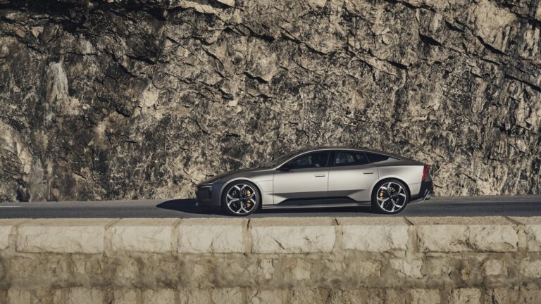 En silverfärgad Polestar 5 kör på en väg bredvid ett berg.